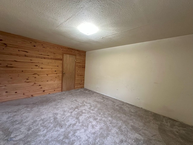 empty room featuring carpet flooring, wood walls, and a textured ceiling