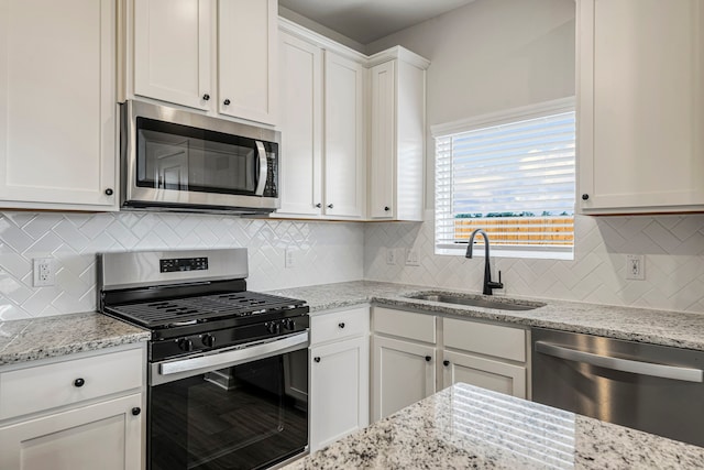kitchen with decorative backsplash, light stone countertops, a sink, stainless steel appliances, and white cabinetry
