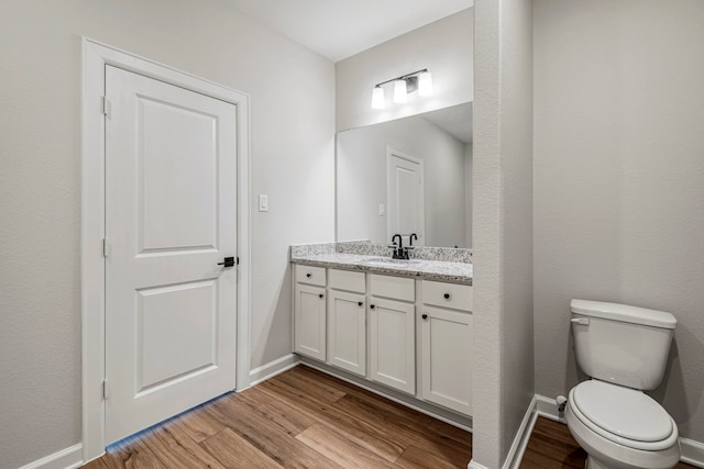 half bathroom with vanity, baseboards, wood finished floors, and toilet