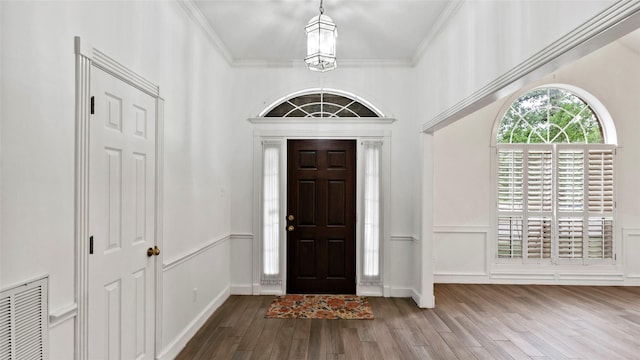 entrance foyer featuring visible vents, wood finished floors, a wainscoted wall, ornamental molding, and a decorative wall