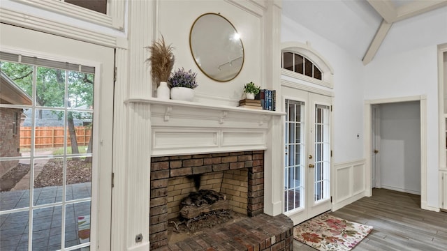 living room with wainscoting, a brick fireplace, wood finished floors, a decorative wall, and french doors