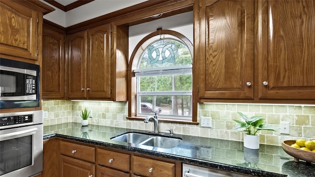 kitchen featuring a sink, dark stone countertops, appliances with stainless steel finishes, and decorative backsplash