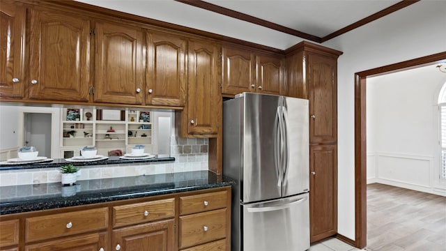 kitchen with freestanding refrigerator, dark stone counters, brown cabinets, and ornamental molding