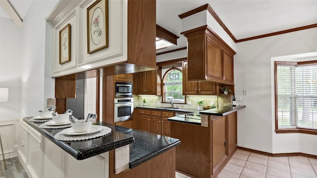 kitchen with brown cabinetry, a peninsula, a sink, appliances with stainless steel finishes, and backsplash