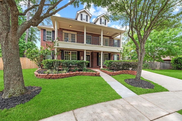view of front of property with fence, brick siding, a front yard, a balcony, and covered porch