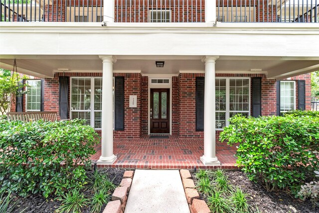 entrance to property with a balcony, a porch, and brick siding