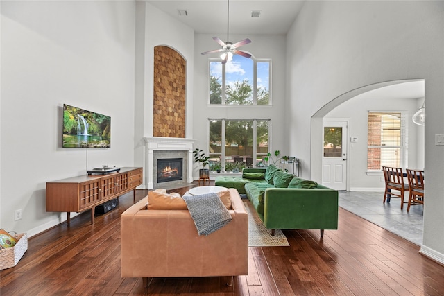 living room with ceiling fan, a high ceiling, arched walkways, dark wood finished floors, and a fireplace with flush hearth