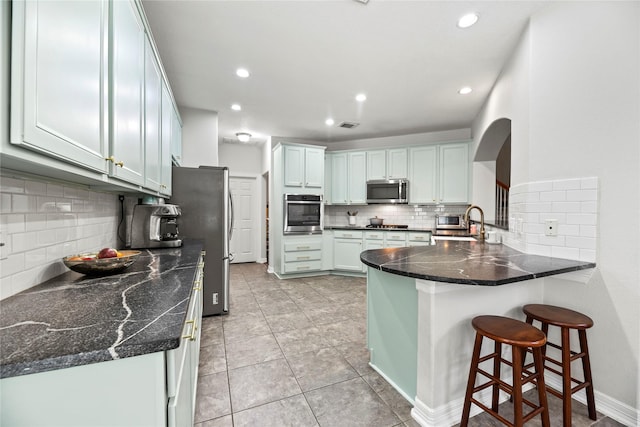 kitchen with a breakfast bar, arched walkways, stainless steel appliances, a peninsula, and backsplash