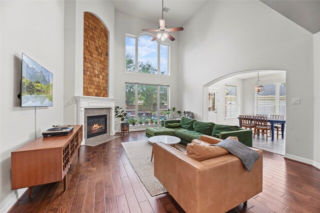 living area featuring a fireplace with flush hearth, a high ceiling, dark wood-style floors, arched walkways, and a ceiling fan