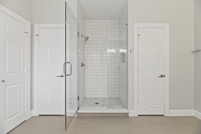 full bath featuring tile patterned floors, baseboards, and a shower stall