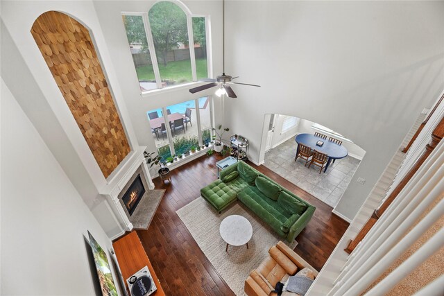 living room featuring wood-type flooring, arched walkways, a tiled fireplace, a ceiling fan, and a towering ceiling