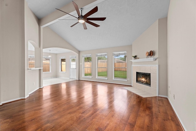 1635 Ashton Village Dr, Spring, TX 77386 - unfurnished living room with ceiling fan, arched walkways, a fireplace, wood finished floors, and high vaulted ceiling