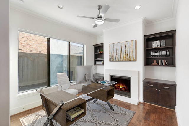 office area with ornamental molding, wood finished floors, ceiling fan, a lit fireplace, and recessed lighting