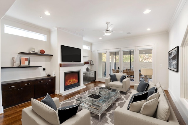 living area with ceiling fan, a lit fireplace, dark wood-style flooring, crown molding, and recessed lighting
