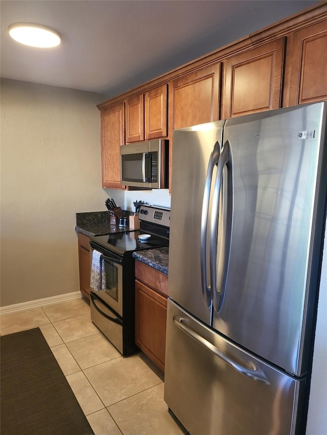 3922 Lakewood Dr, Montgomery, TX 77356 - kitchen featuring brown cabinetry, dark stone counters, stainless steel appliances, baseboards, and light tile patterned floors