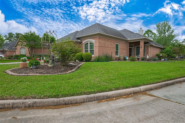 view of front facade with brick siding, a chimney, a front yard, and roof with shingles