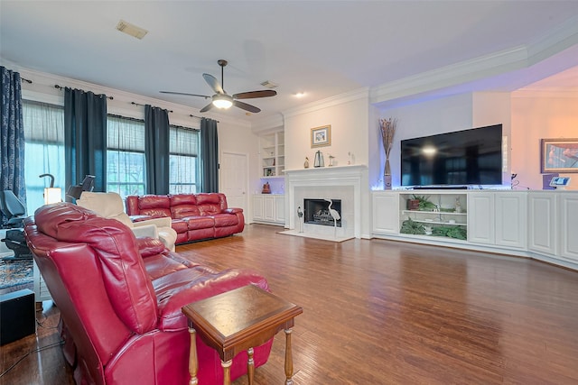 living area with a ceiling fan, visible vents, crown molding, a tiled fireplace, and wood finished floors