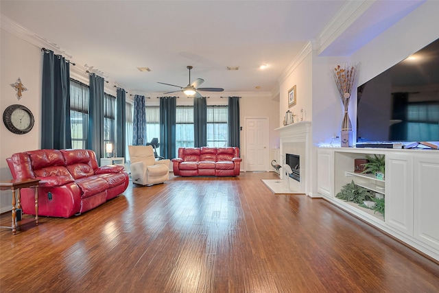 living area with crown molding, a fireplace with flush hearth, ceiling fan, and wood finished floors