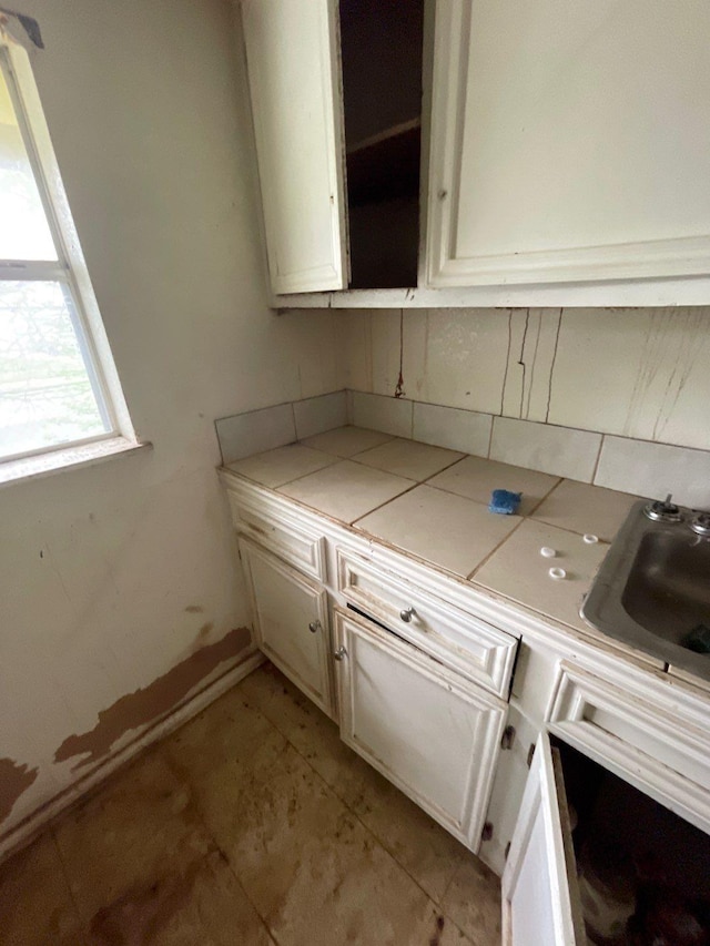 kitchen featuring decorative backsplash, open shelves, a sink, tile counters, and white cabinetry