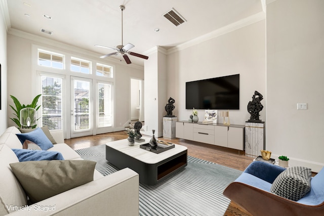 living room with a ceiling fan, visible vents, ornamental molding, and wood finished floors