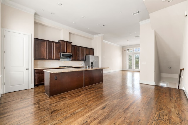 kitchen featuring dark wood-type flooring, ornamental molding, a center island with sink, and stainless steel appliances