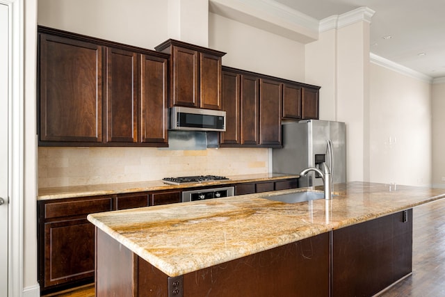 kitchen with ornamental molding, a kitchen island with sink, tasteful backsplash, a sink, and stainless steel appliances