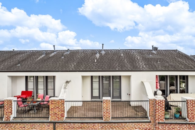 back of property featuring brick siding, roof with shingles, and stucco siding