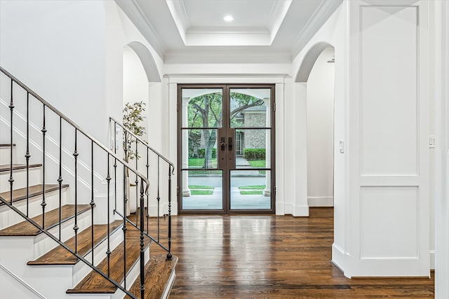 entrance foyer with ornamental molding, dark wood-type flooring, a tray ceiling, french doors, and arched walkways