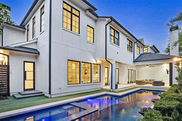 rear view of property featuring an outdoor living space, a ceiling fan, an outdoor pool, and stucco siding