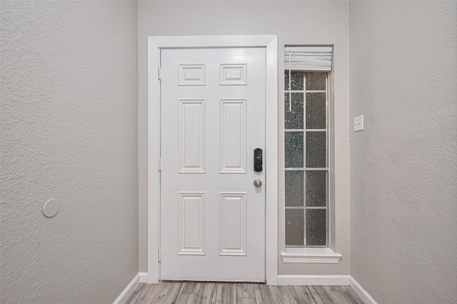 doorway with baseboards, a textured wall, and wood finished floors
