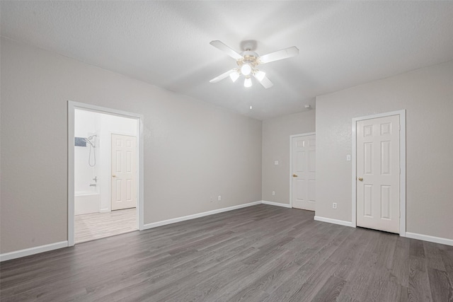 unfurnished bedroom featuring dark wood-style flooring, baseboards, ceiling fan, and ensuite bathroom