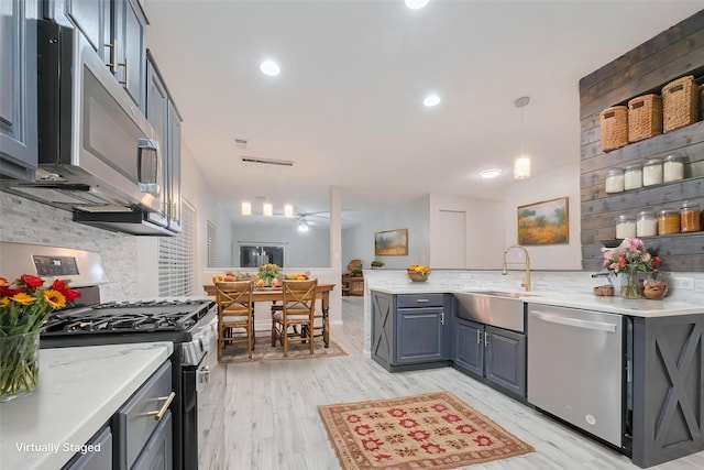 kitchen with hanging light fixtures, a sink, light wood finished floors, stainless steel appliances, and a peninsula