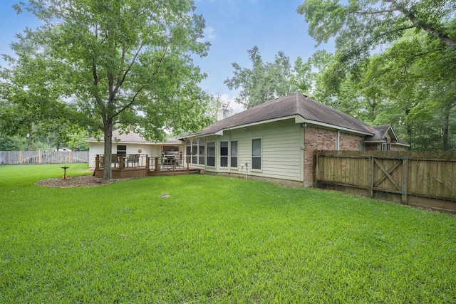 back of house featuring a deck, a fenced backyard, a chimney, brick siding, and a lawn