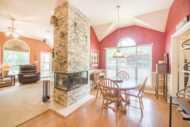 dining area with a ceiling fan, wood finished floors, vaulted ceiling, and a fireplace