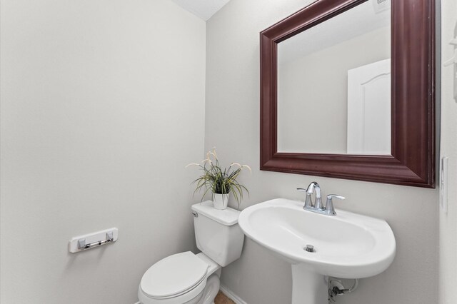 half bath with baseboards, a sink, and toilet