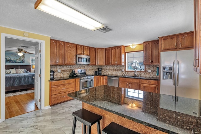 kitchen featuring a textured ceiling, appliances with stainless steel finishes, backsplash, and a breakfast bar
