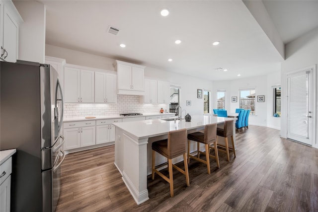 kitchen featuring a kitchen island with sink, stainless steel refrigerator with ice dispenser, visible vents, gas stovetop, and a sink