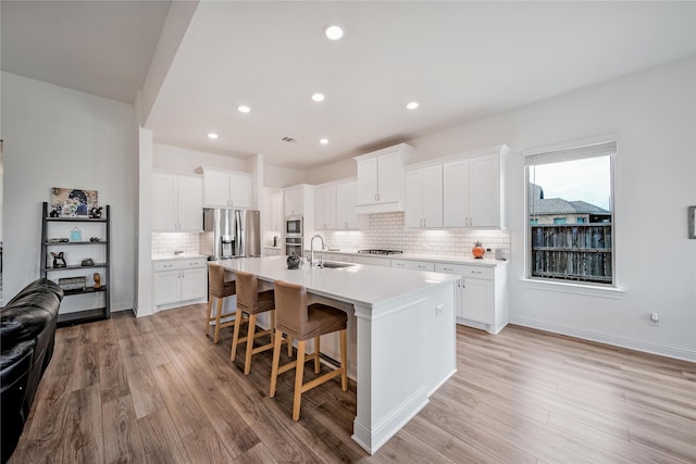 kitchen featuring an island with sink, light countertops, tasteful backsplash, light wood-style flooring, and appliances with stainless steel finishes