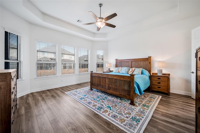 bedroom with baseboards, a tray ceiling, visible vents, and wood finished floors