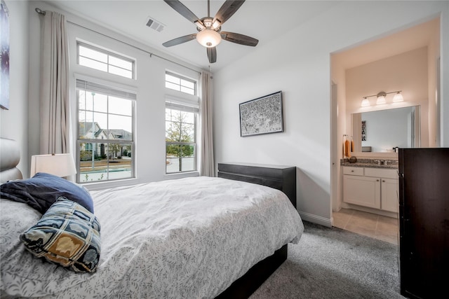 bedroom with ceiling fan, light colored carpet, visible vents, baseboards, and ensuite bathroom