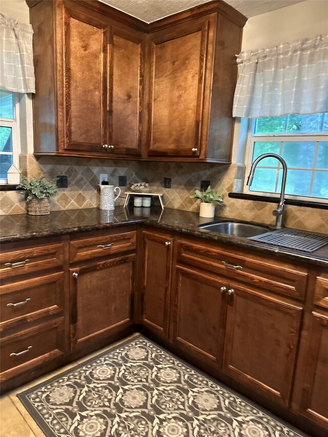 kitchen with a sink, dark stone counters, a healthy amount of sunlight, and tasteful backsplash