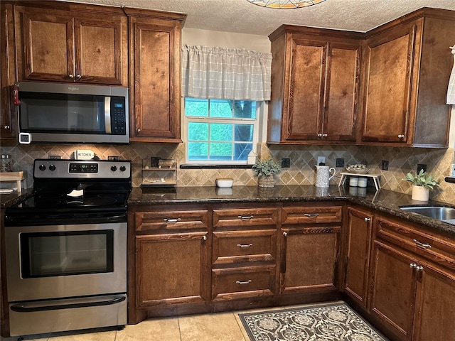 kitchen featuring decorative backsplash, dark stone counters, a sink, appliances with stainless steel finishes, and light tile patterned floors