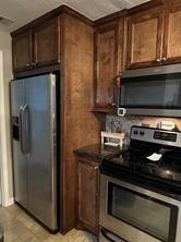 kitchen with stainless steel appliances, dark countertops, and dark brown cabinets