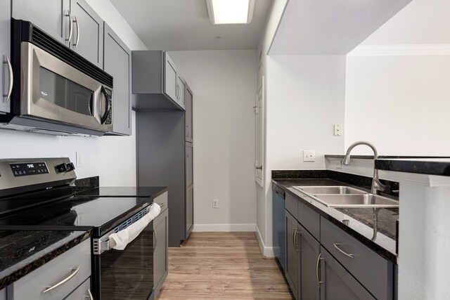 kitchen featuring dark stone counters, a sink, light wood-style flooring, gray cabinetry, and stainless steel appliances