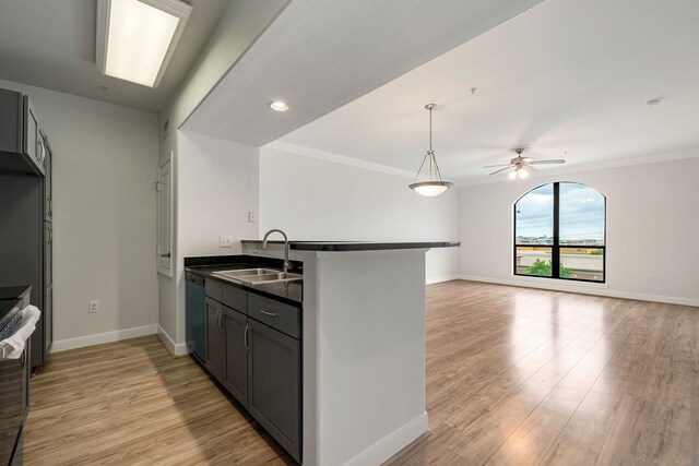 kitchen featuring dark countertops, a sink, baseboards, a peninsula, and light wood-style flooring
