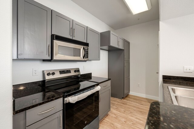 kitchen featuring a sink, dark stone countertops, light wood finished floors, gray cabinetry, and stainless steel appliances
