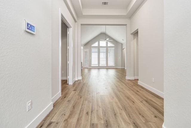 corridor featuring visible vents, baseboards, lofted ceiling, a textured wall, and light wood-style flooring