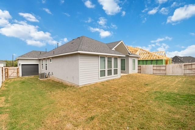 back of house featuring an attached garage, central AC unit, a fenced backyard, and a yard