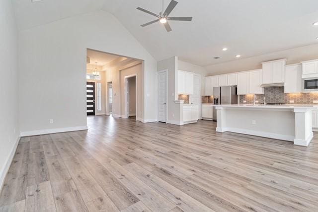 unfurnished living room featuring recessed lighting, vaulted ceiling, light wood finished floors, and ceiling fan with notable chandelier