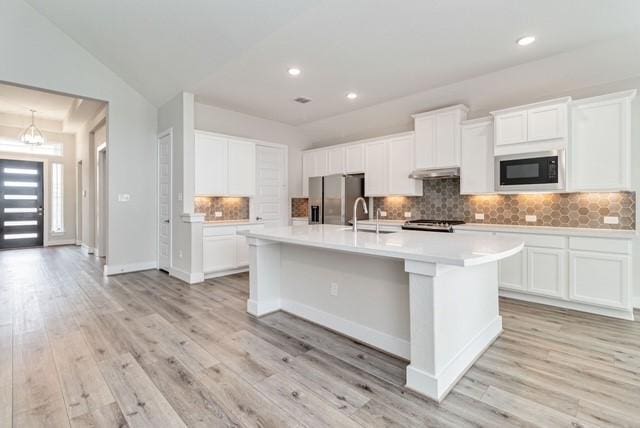 kitchen featuring decorative backsplash, a kitchen island with sink, black microwave, light countertops, and stainless steel fridge with ice dispenser
